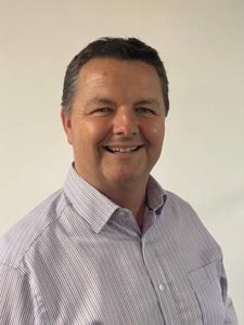 Middle-aged man smiling at camera wearing light purple striped button-up shirt