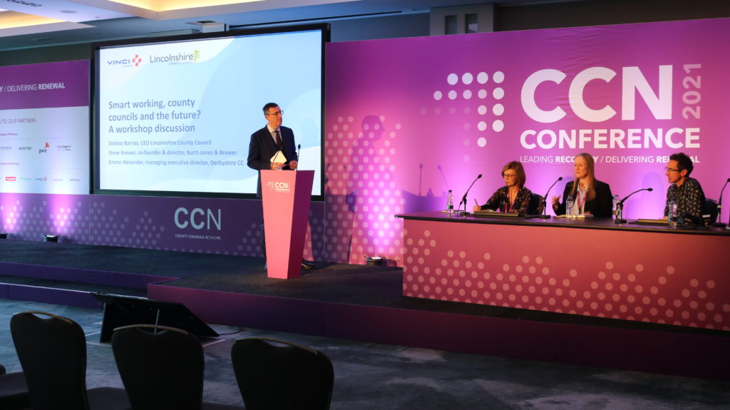 Speaker presenting at CCN 2021 Conference with panel members seated at table.
