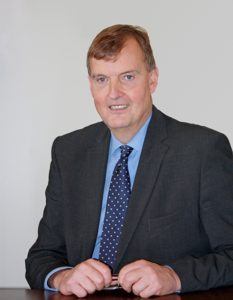 Professional headshot of middle-aged man in dark suit and blue tie