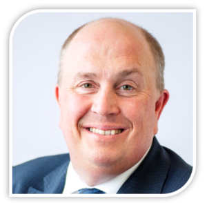 Professional headshot of a smiling bald man wearing a dark blue suit and tie