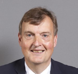 Professional headshot of middle-aged man with brown hair wearing dark suit and white shirt
