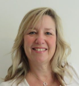 Portrait of a smiling woman with blonde wavy hair against a light gray background