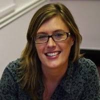 Woman with long hair and glasses smiling at camera indoors