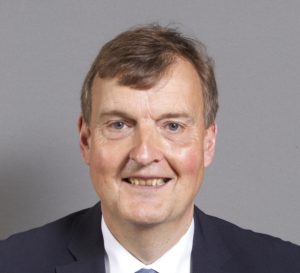 Middle-aged man in dark suit and white shirt smiling at camera against gray background