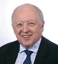 Professional headshot of an older man in a dark suit and tie, smiling