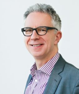 Portrait of smiling middle-aged man with gray hair wearing glasses and blazer.