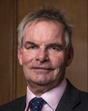 Middle-aged man in dark suit and purple tie against wooden background.