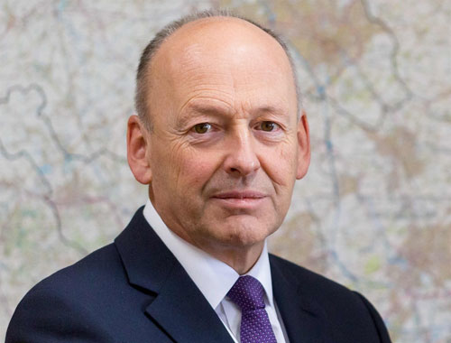 Middle-aged man in dark suit and purple tie against map background