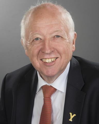 Older man in dark suit and red tie smiling at camera, professional headshot portrait.