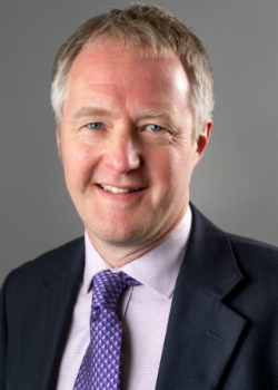 Professional headshot of smiling middle-aged man in dark suit and purple tie.