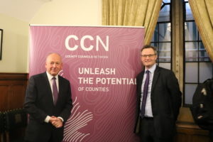 Two men in suits stand beside a CCN banner promoting unleashing potential of countries.