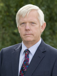 Older man with white hair wearing navy blazer and patterned tie
