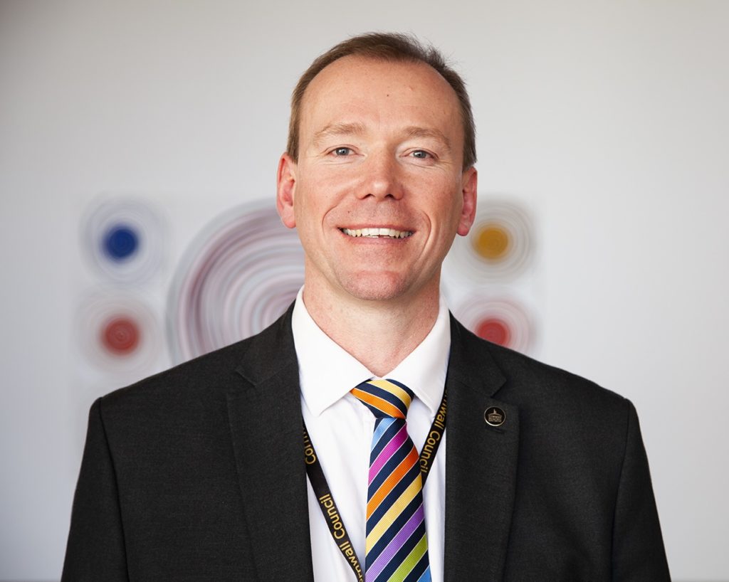 Smiling middle-aged man in black suit and colorful striped tie against white background.