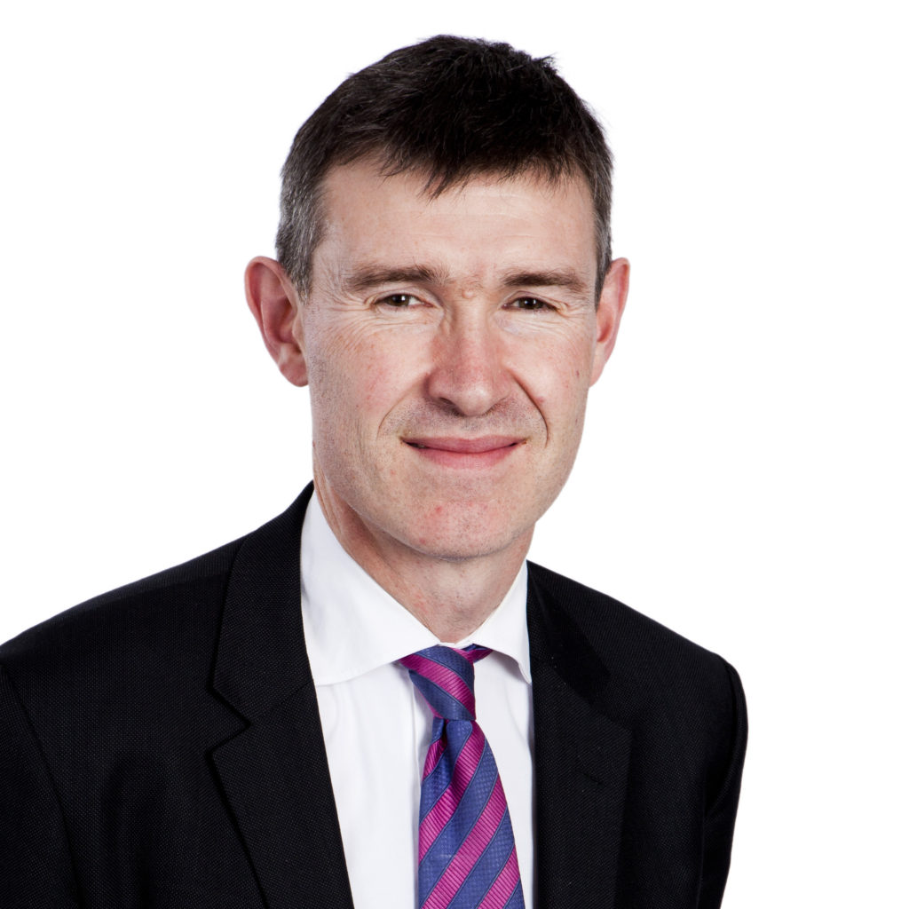 Professional headshot of man wearing black blazer and striped tie