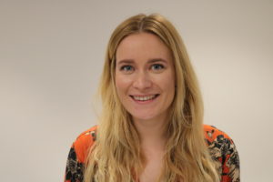 Smiling woman with long blonde hair wearing colorful patterned orange and dark top