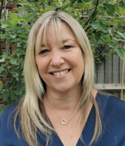 Smiling woman with blonde hair and bangs wearing dark blue top outdoors