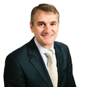 Professional headshot of smiling man wearing dark blazer and striped tie