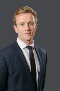Professional portrait of a man in dark business suit and tie on gray background