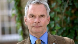 Older man with gray hair in blue shirt and brown jacket portrait outdoors