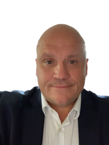 Bald man in dark blazer and white shirt smiling at camera headshot