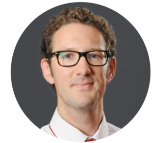 Professional headshot of man with curly hair and glasses wearing white shirt