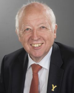 Smiling older man with white hair wearing dark suit and red tie