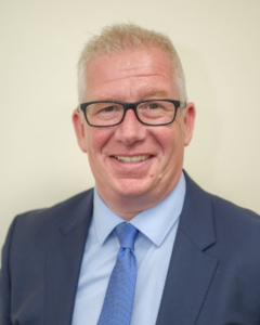 Professional headshot of a smiling middle-aged man wearing glasses and blue suit