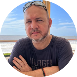 Man with glasses on head wearing black shirt poses at beach outdoors