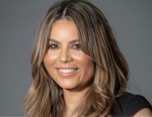 Woman with long wavy brown hair smiling at camera against gray background