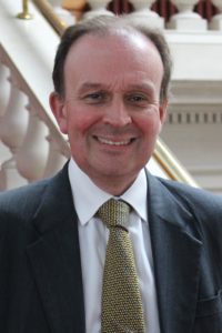 Professional headshot of smiling man in dark suit and green tie indoors.