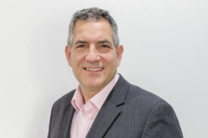 Middle-aged man with gray hair wearing dark blazer and pink shirt smiling at camera