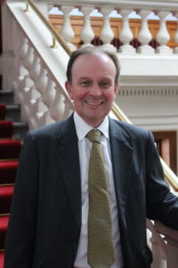 Man in dark suit and tie smiling in front of ornate building with red carpet