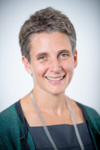 Portrait of smiling woman with short gray hair wearing dark cardigan and lanyard