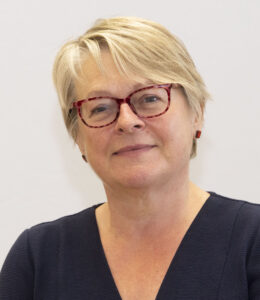 Middle-aged woman with short blonde hair and purple glasses wearing dark top.
