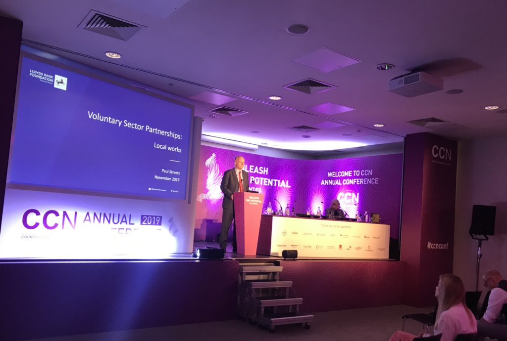 Speaker at podium during CCN Annual Conference 2019 with purple lighting and "Unleash Potential" backdrop display