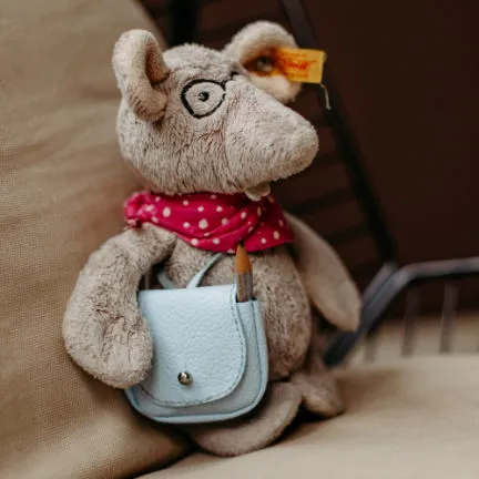 Stuffed animal Liesel Leseratte wearing glasses, a pink polka-dot scarf, and a small blue bag with a pencil. She looks very sophisticated and helps Louisa Hoffschult as her personal assistant and source of inspiration.