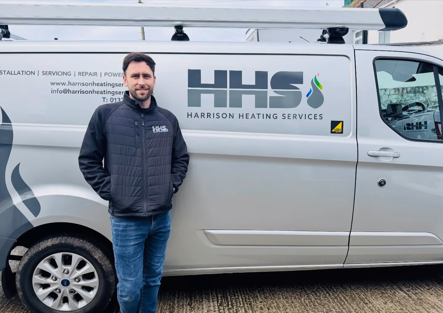 A man stands next to a van with "Harrison Heating Services" written on the side.