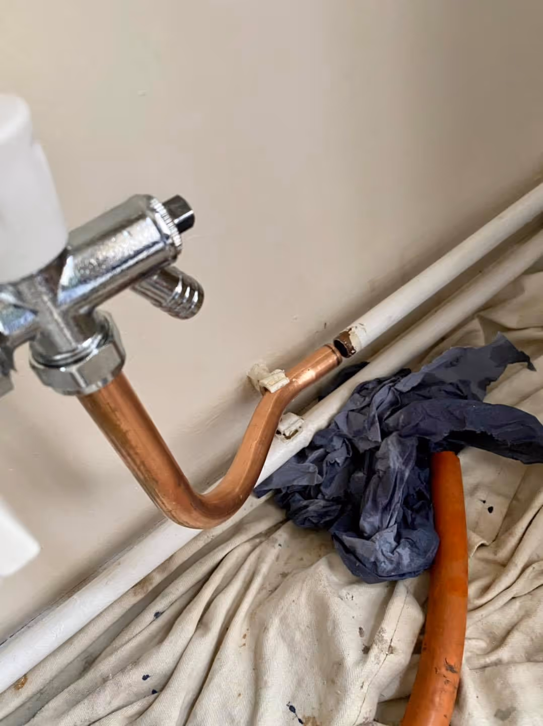 Copper pipes connected to a wall with a towel and a hose on the floor nearby.