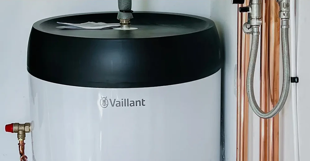 A white water heater with copper pipes attached, positioned against a wall.