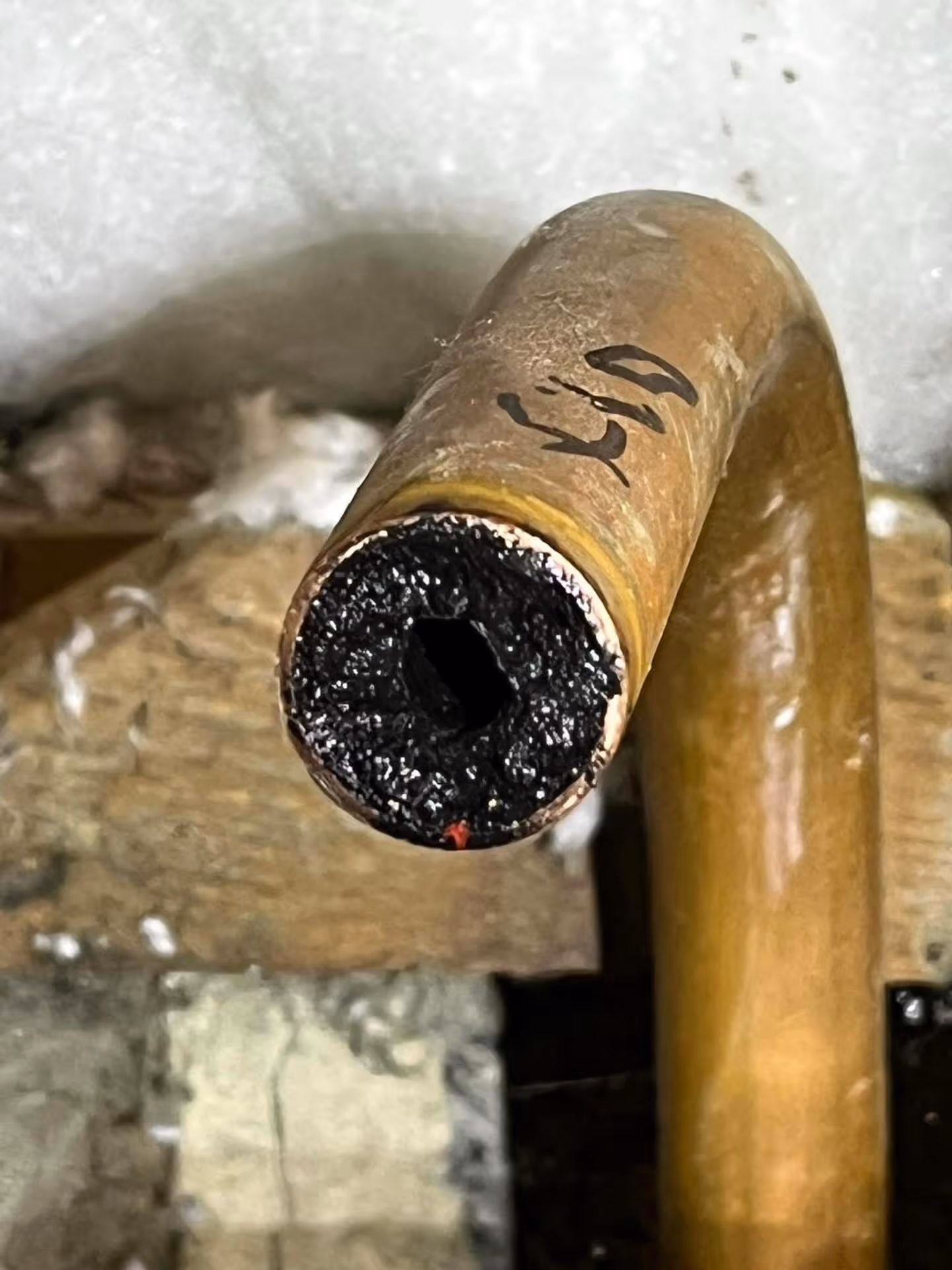 Close-up of a partially clogged pipe with dark residue inside the opening.