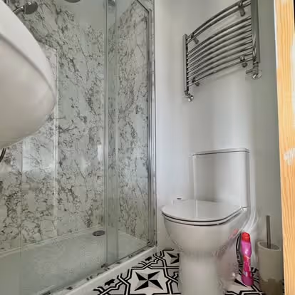 Bathroom with a toilet, a walk-in shower, and a patterned floor. A towel rack is on the wall.