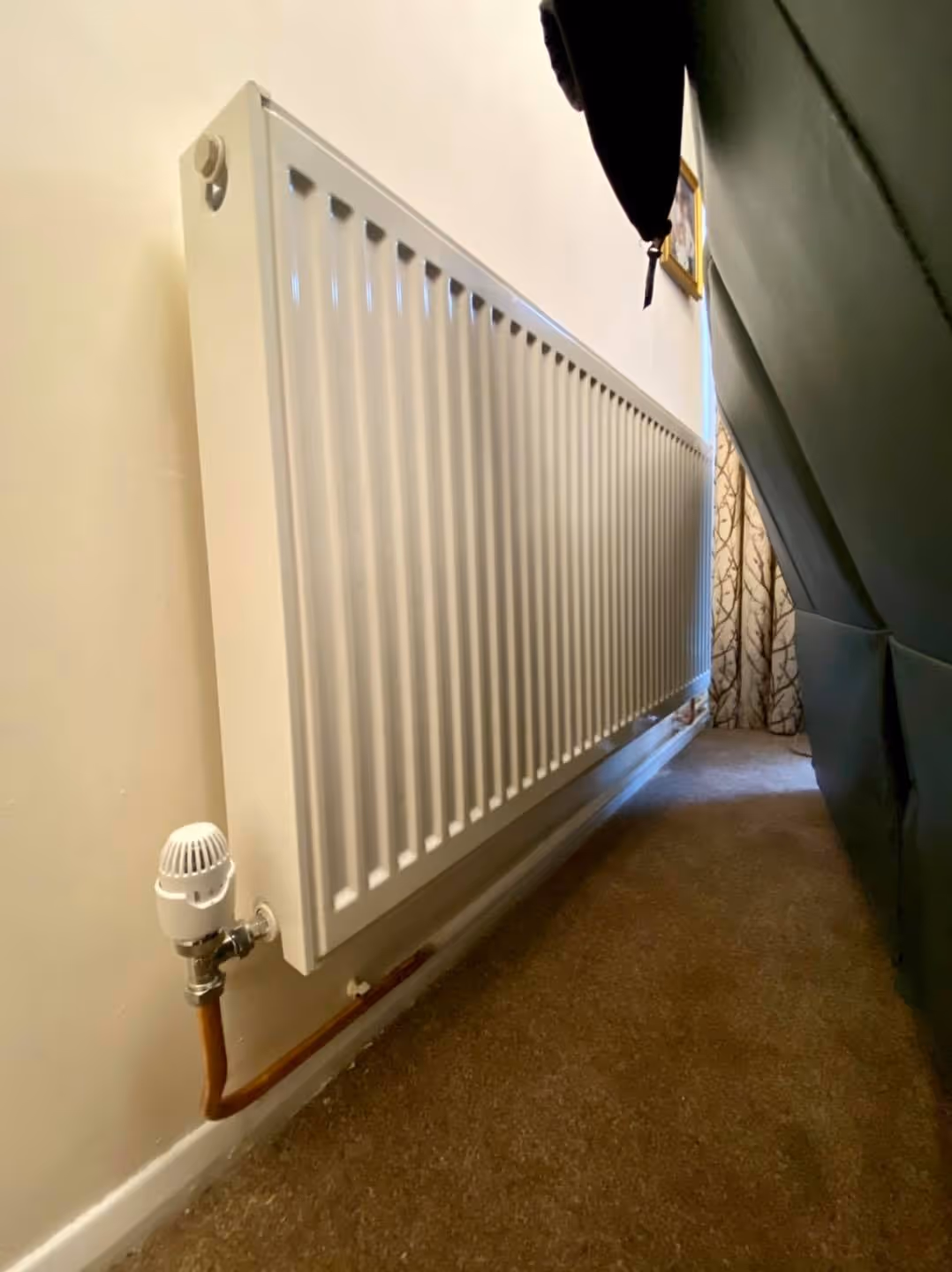 A white radiator is mounted on a wall, with a sofa partially in the foreground.