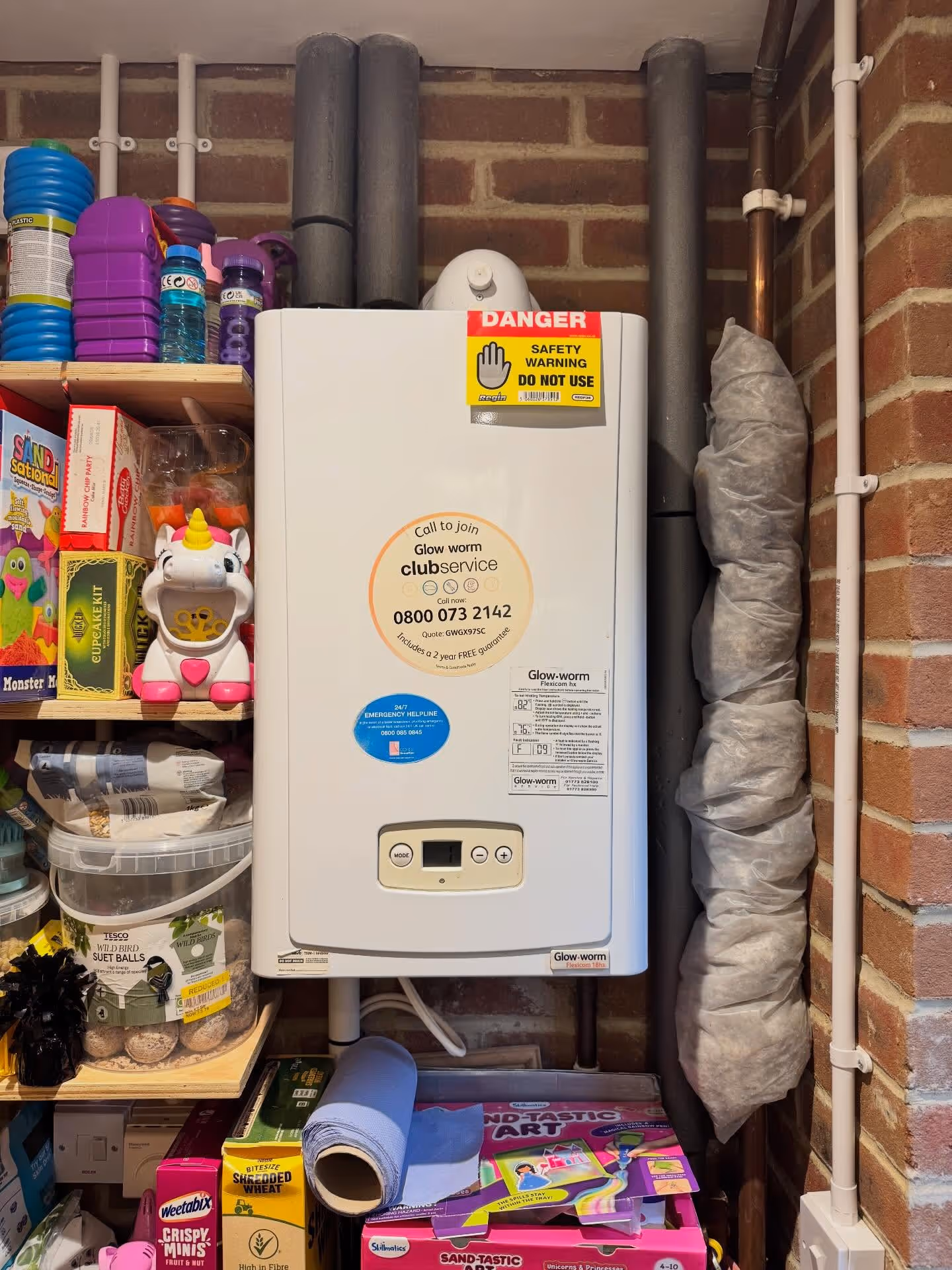 A white boiler is installed on a wall, surrounded by shelves with toys and supplies.