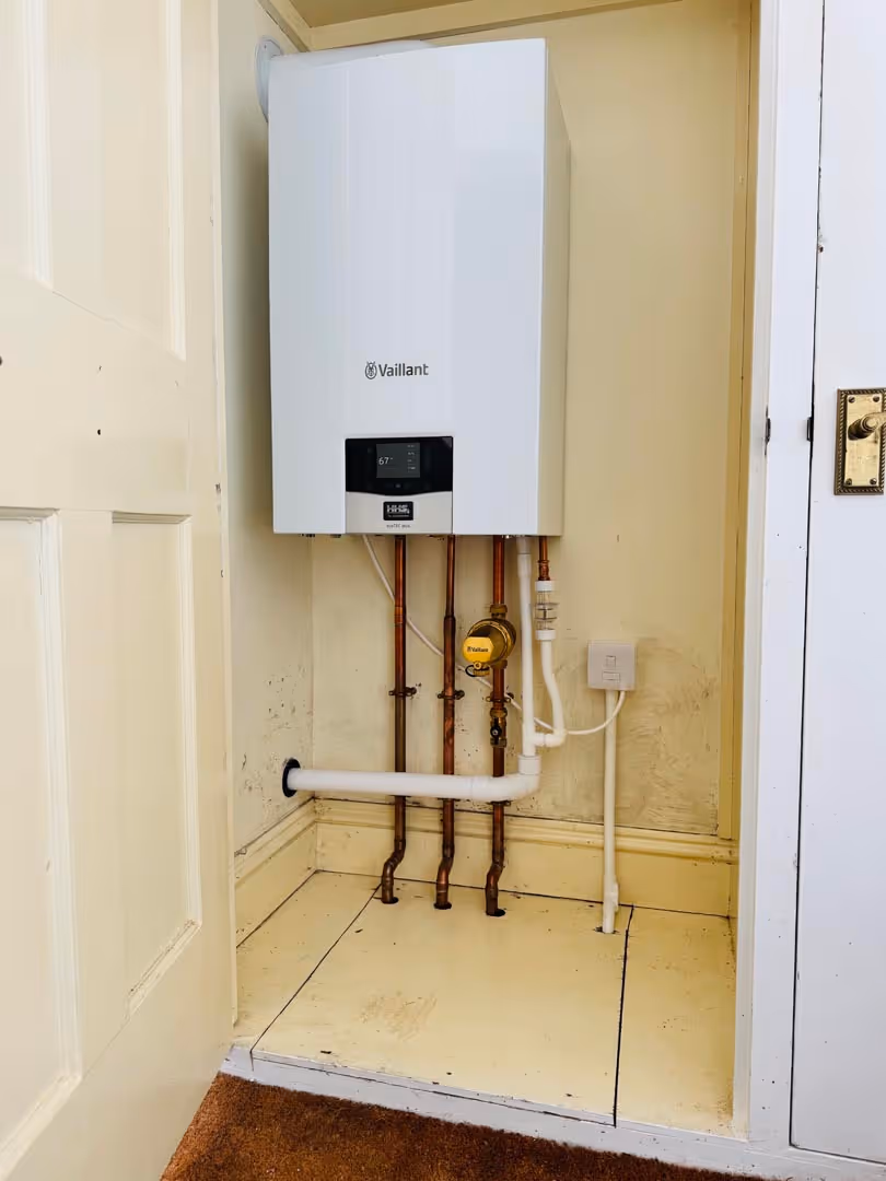 A white boiler is mounted on a wall with visible pipes underneath.