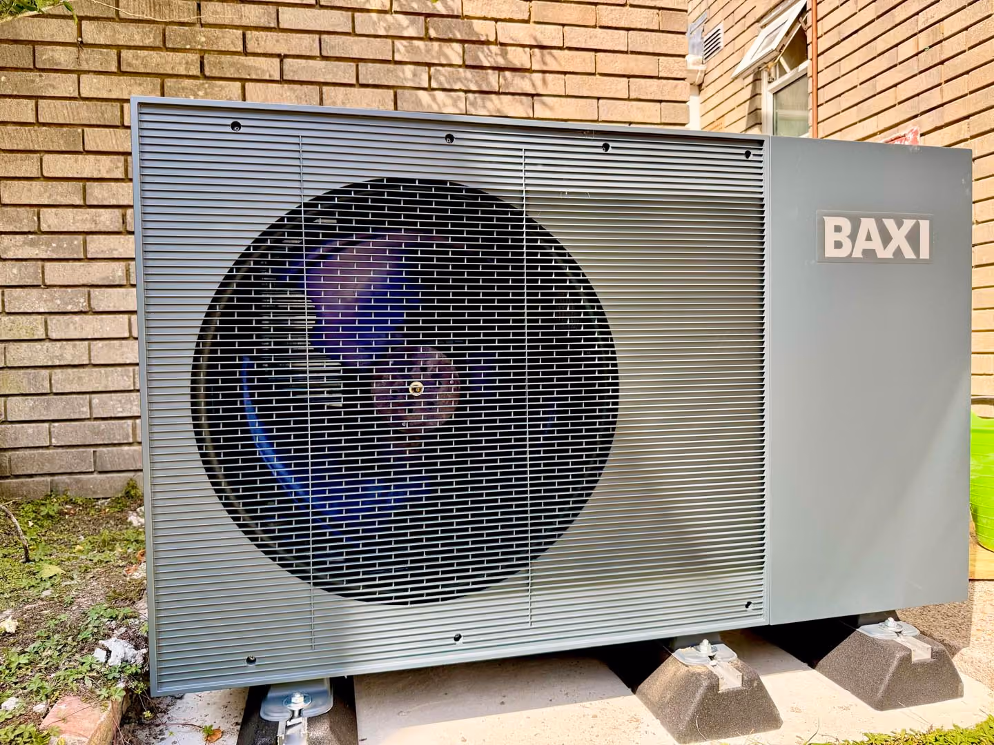 A large outdoor air conditioning unit is mounted on concrete blocks near a brick wall.