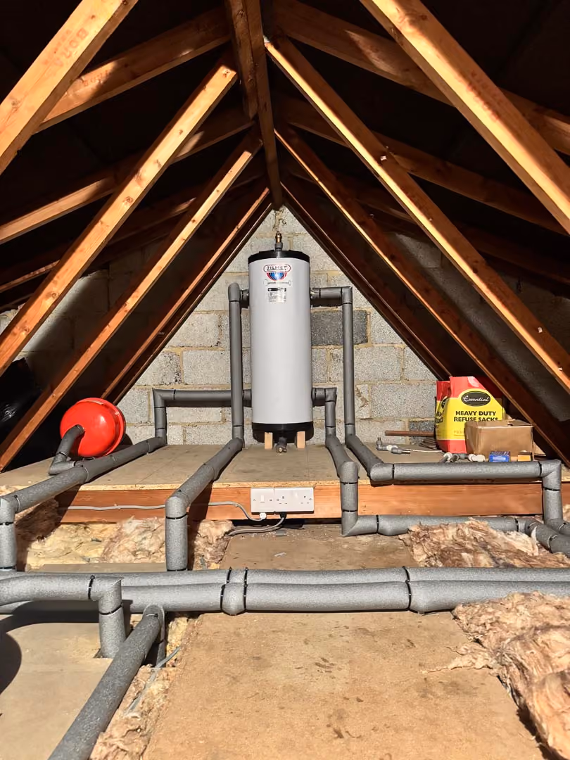 A hot water tank installed in an attic with surrounding insulation and visible piping.