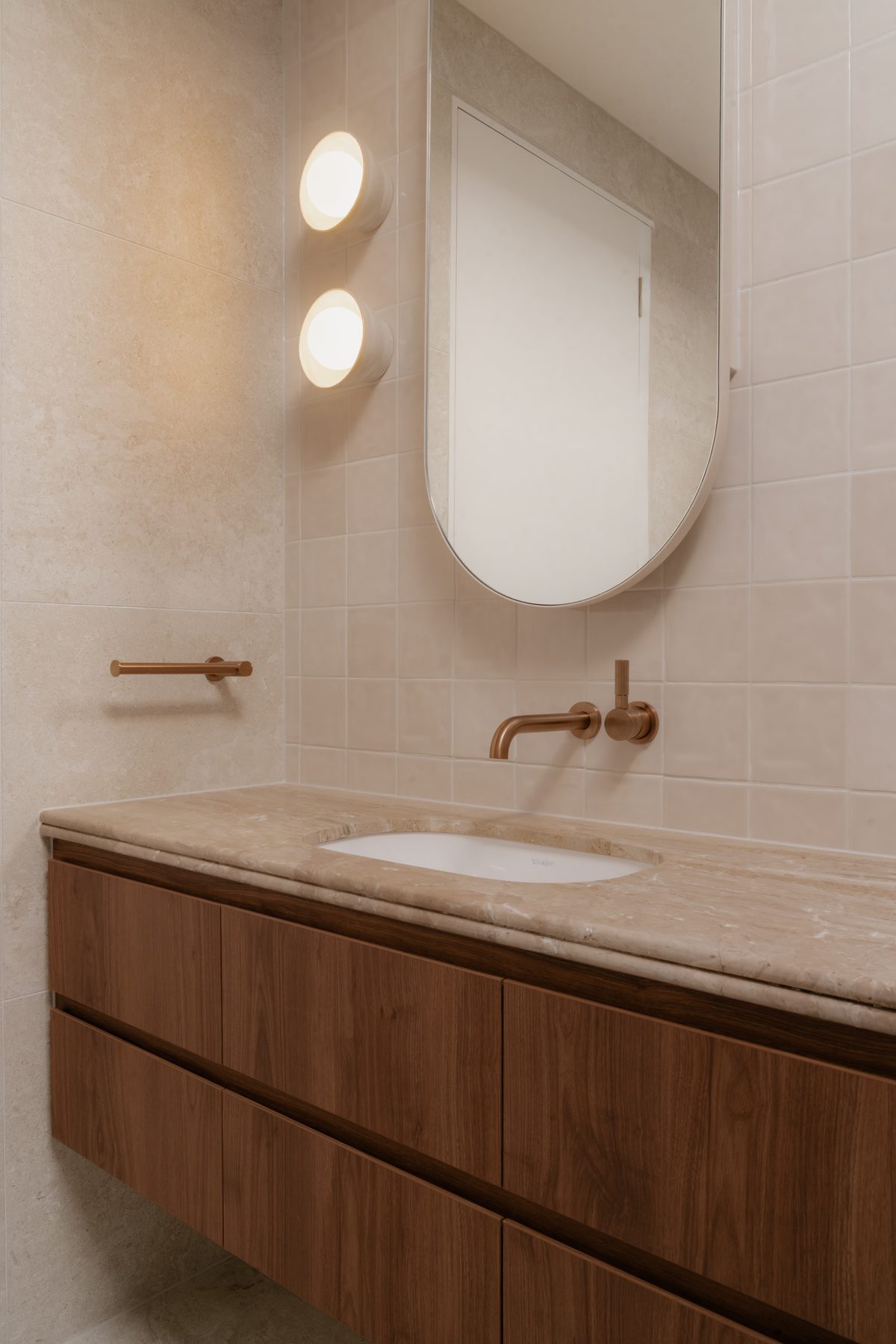 Toorak House ensuite with stone benchtop, walnut vanity, oval mirror, brass tapware and globe wall sconces, Toorak Victoria