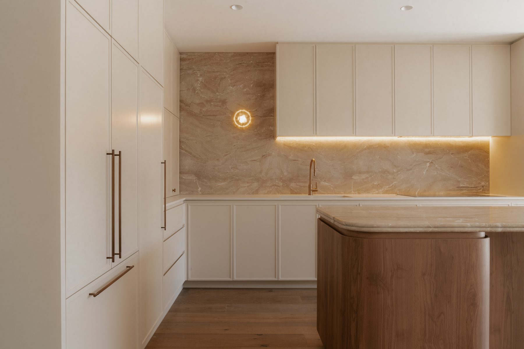 Toorak House kitchen detail with white cabinetry, bronze bar handles and veined stone splashback with warm recessed lighting