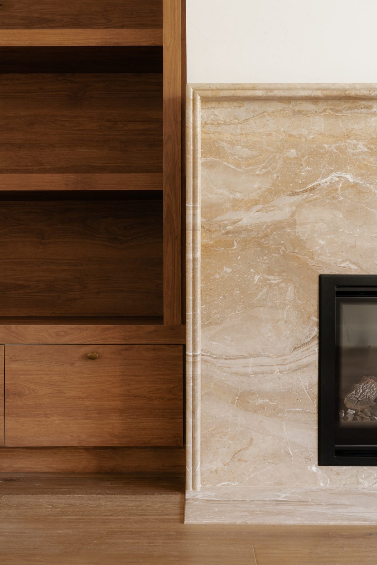 Toorak House fireplace detail with warm veined stone surround and walnut bookcase beside gas insert, interior design by Tote Design Studio