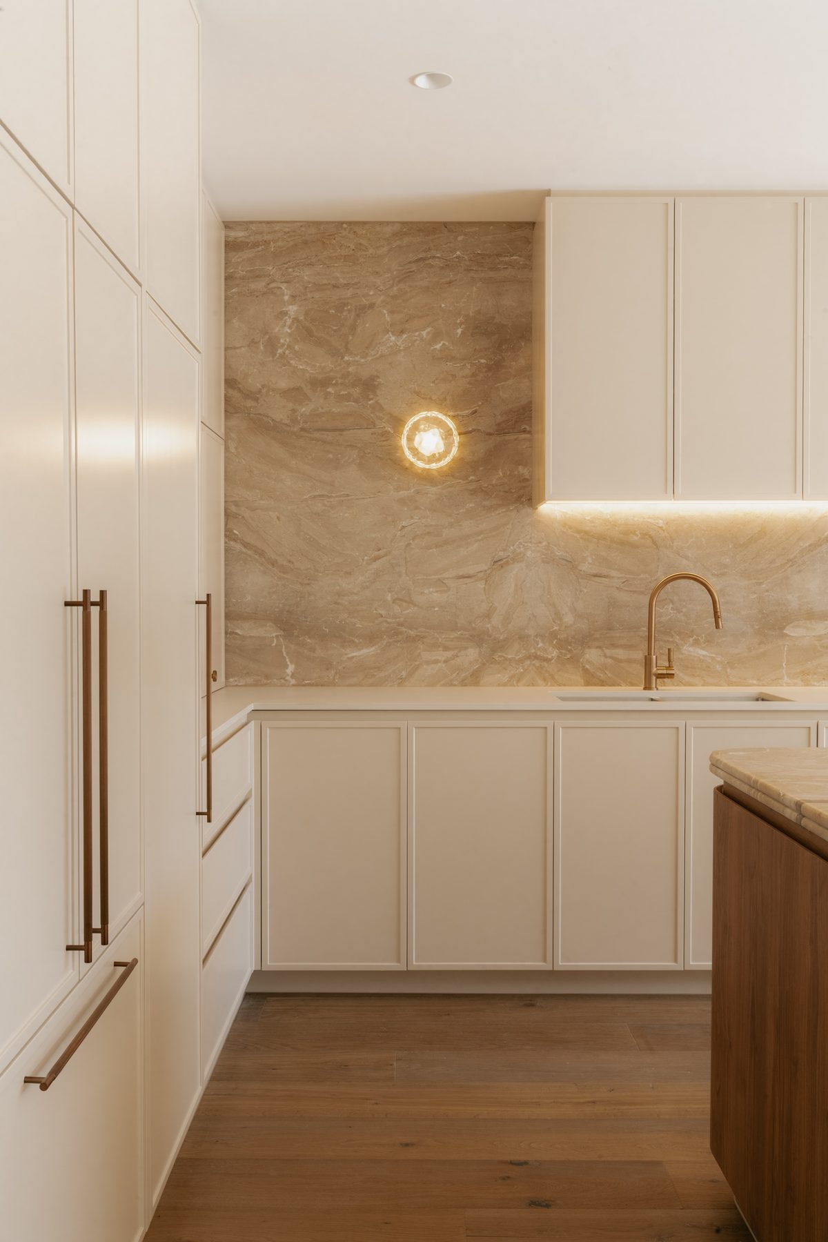 Toorak House kitchen with full height veined stone splashback, wall sconce, cream cabinetry and brass tap, interior design by Tote Design Studio
